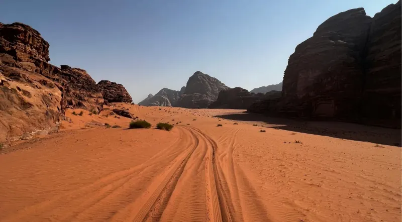 Jeep tracks running through red sand between sandstone massifs in Wadi Rum